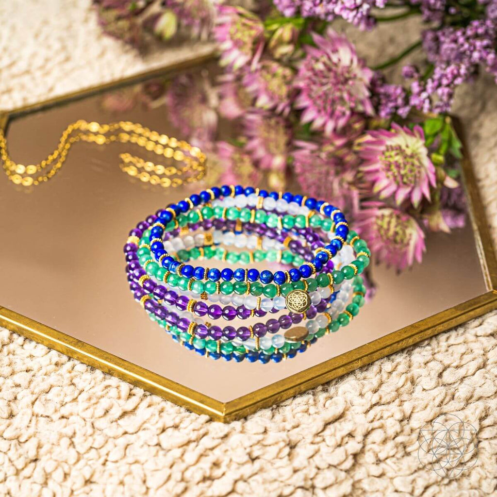 Stack of colorful beaded bracelets on a reflective surface with flowers in the background