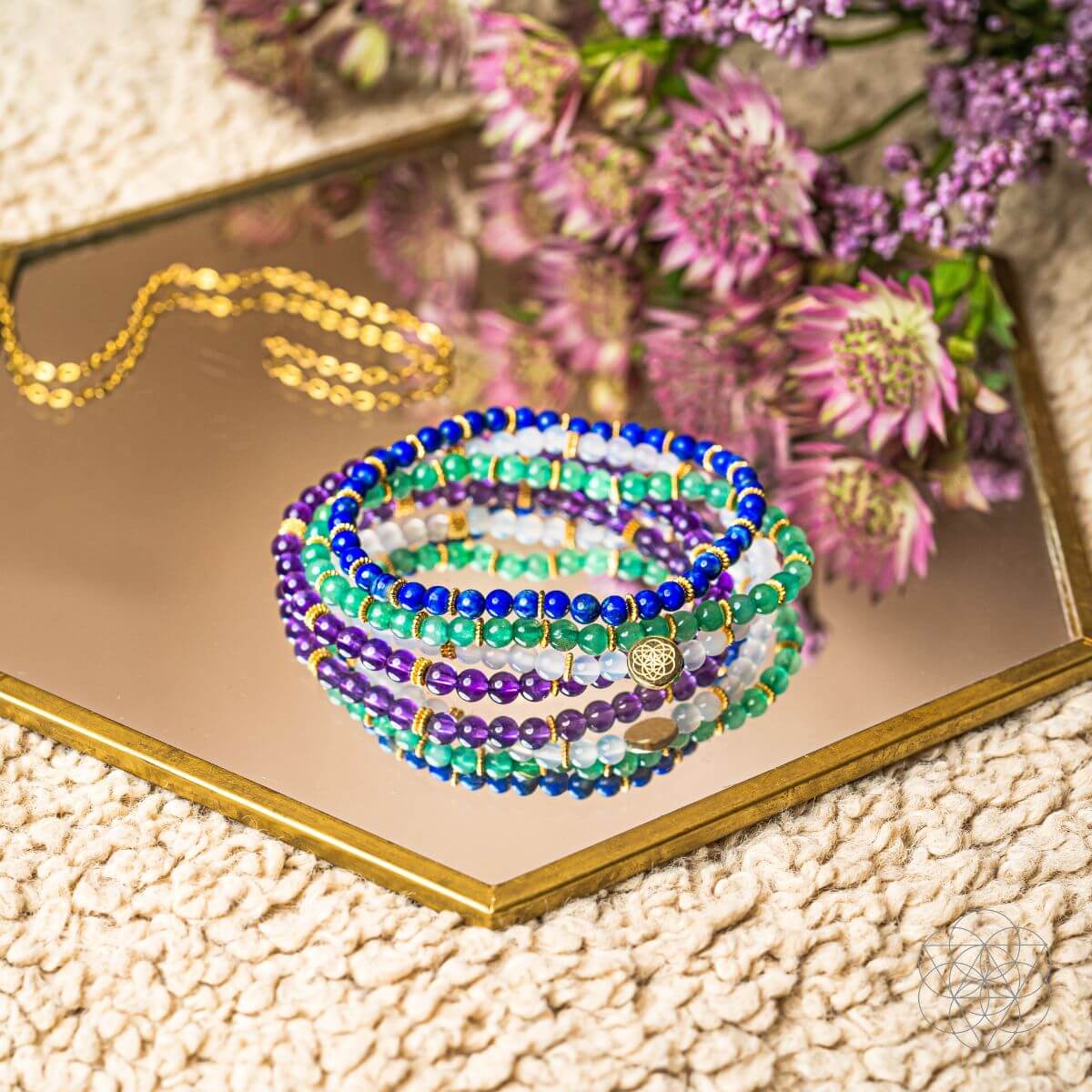 Stack of colorful beaded bracelets on a reflective surface with flowers in the background