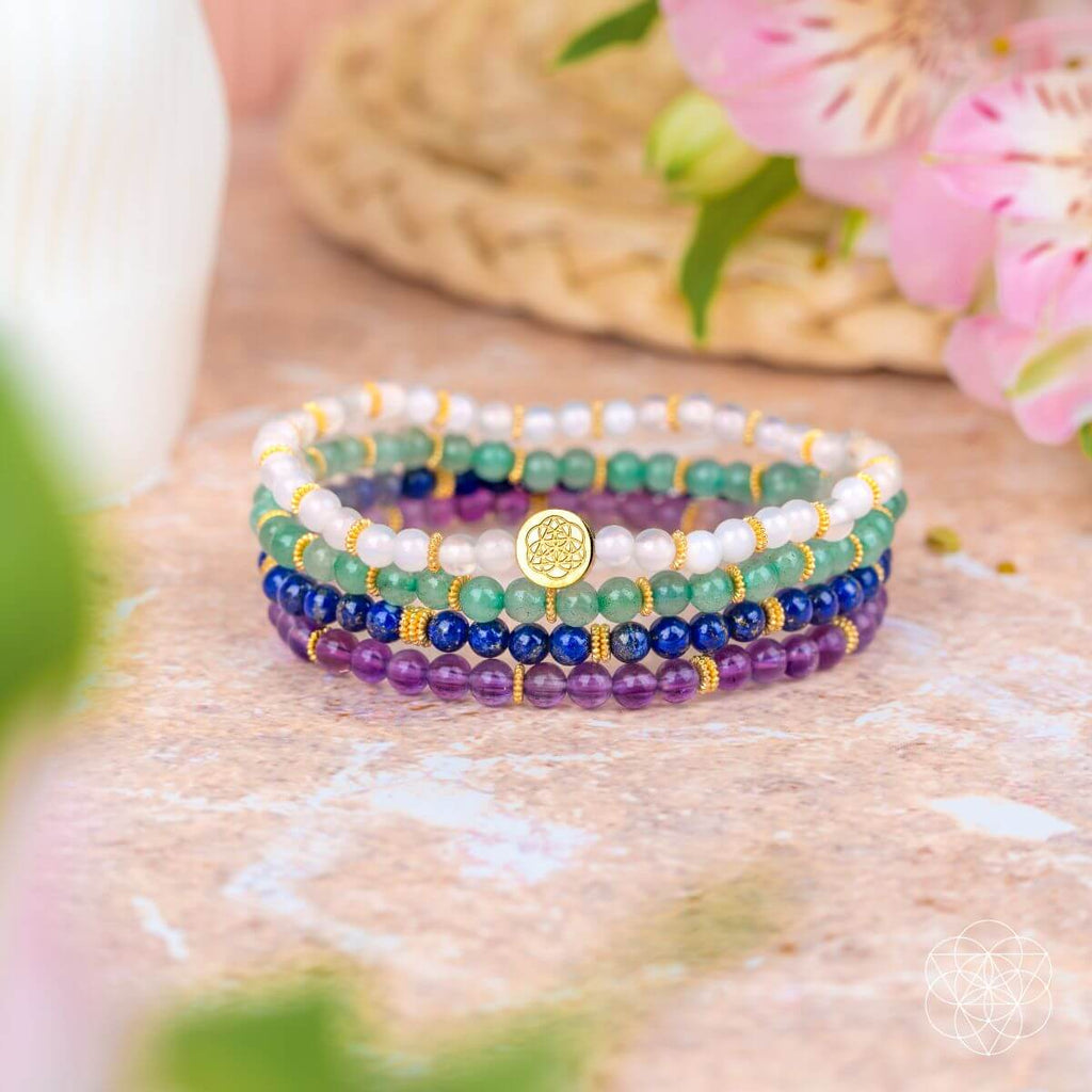 Stack of colorful beaded bracelets on a textured surface with flowers in the background