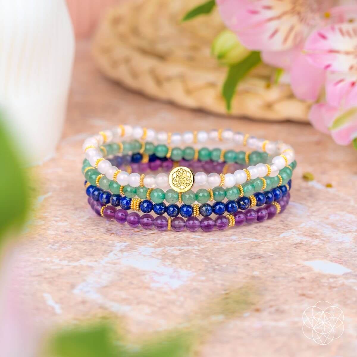 Stack of colorful beaded bracelets on a textured surface with flowers in the background
