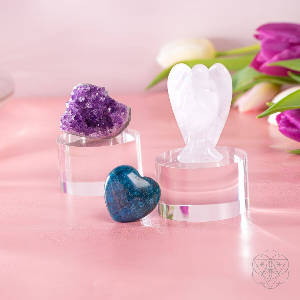 Decorative items including a purple crystal, blue stone, and white angel figure on a pink surface with flowers in the background.