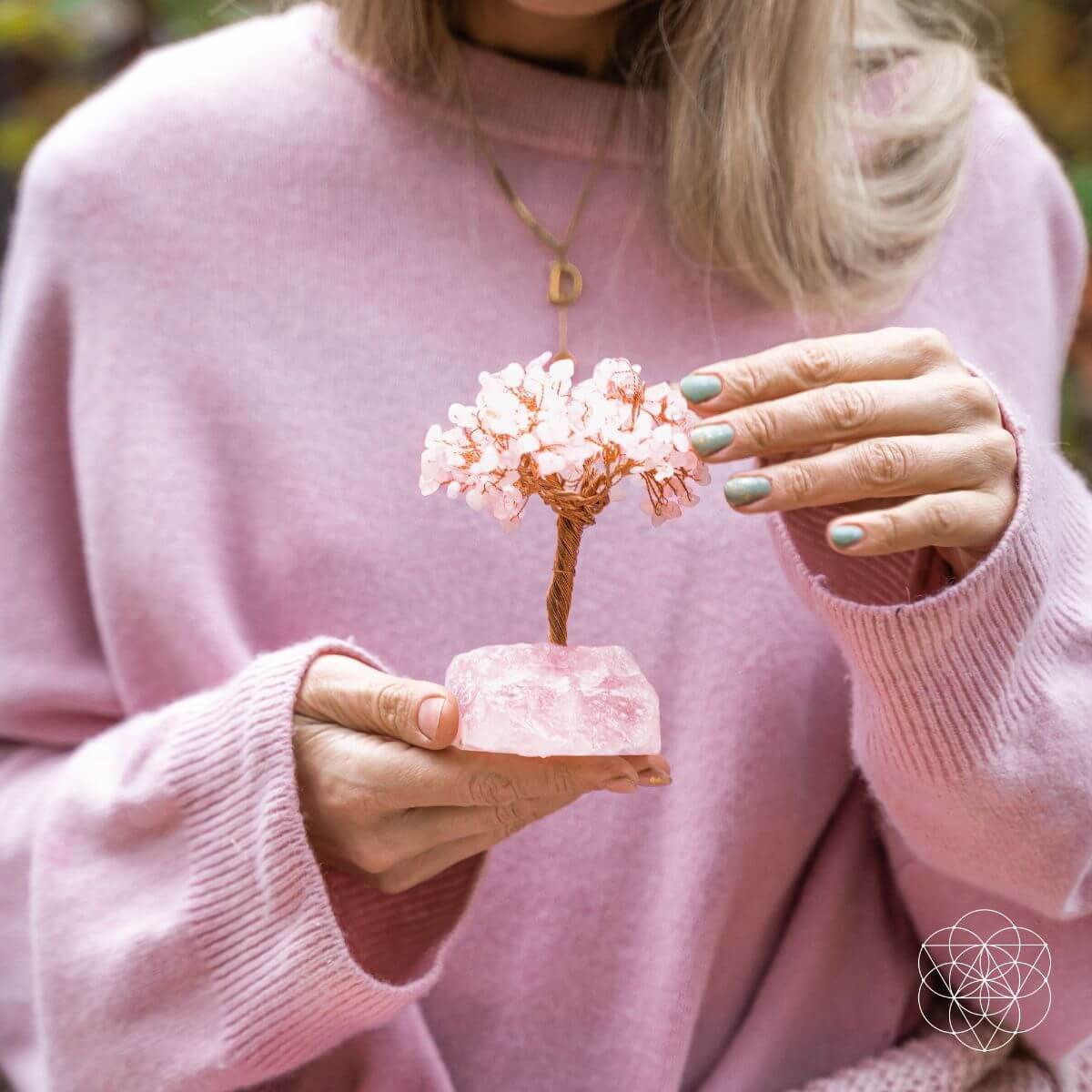 Person wearing a pink sweater holding a small decorative tree with pink flowers.