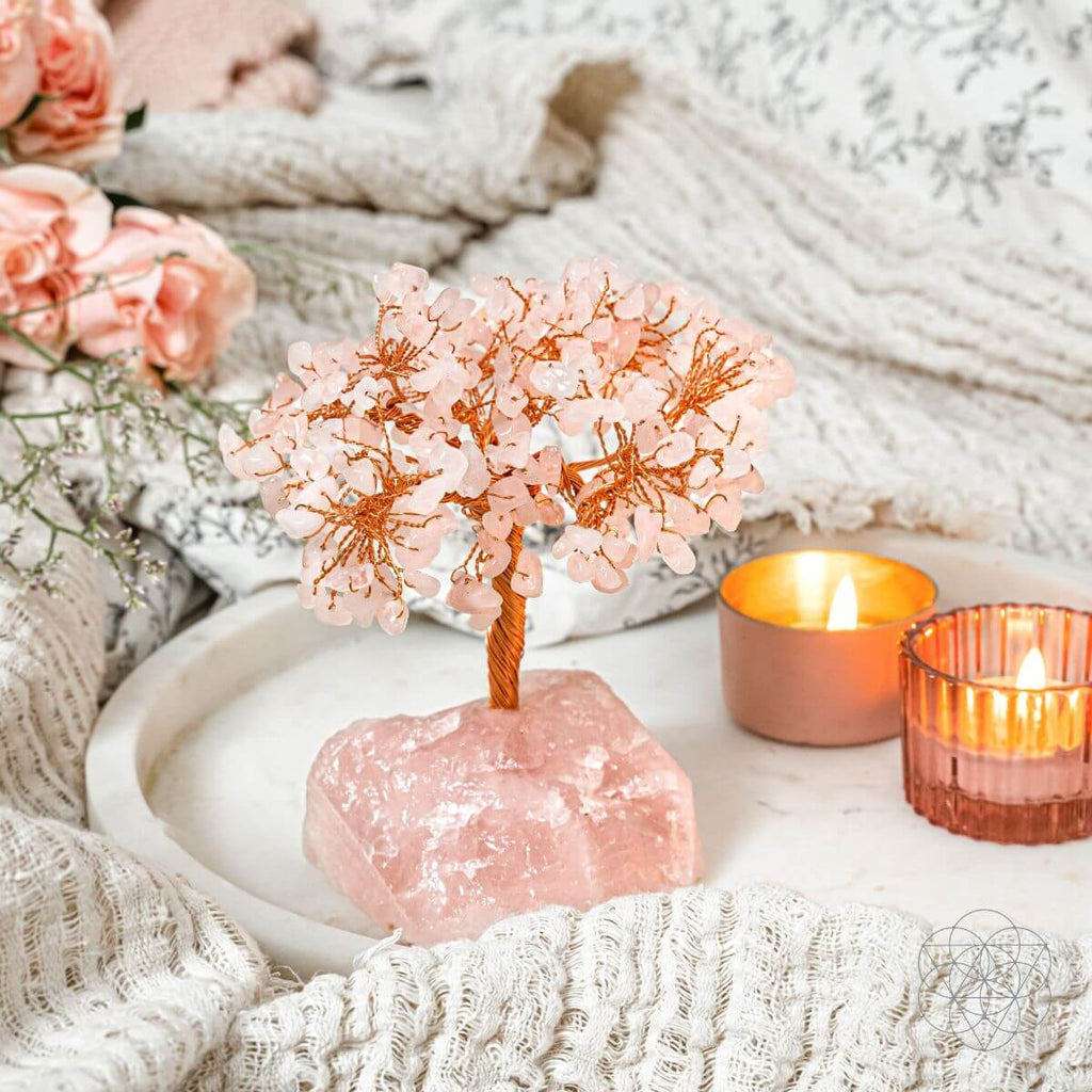 Decorative pink crystal tree on a rock with candles and flowers in the background