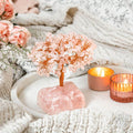 Decorative pink crystal tree on a rock with candles and flowers in the background