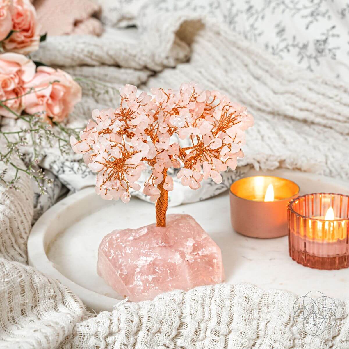 Decorative pink crystal tree on a rock with candles and flowers in the background
