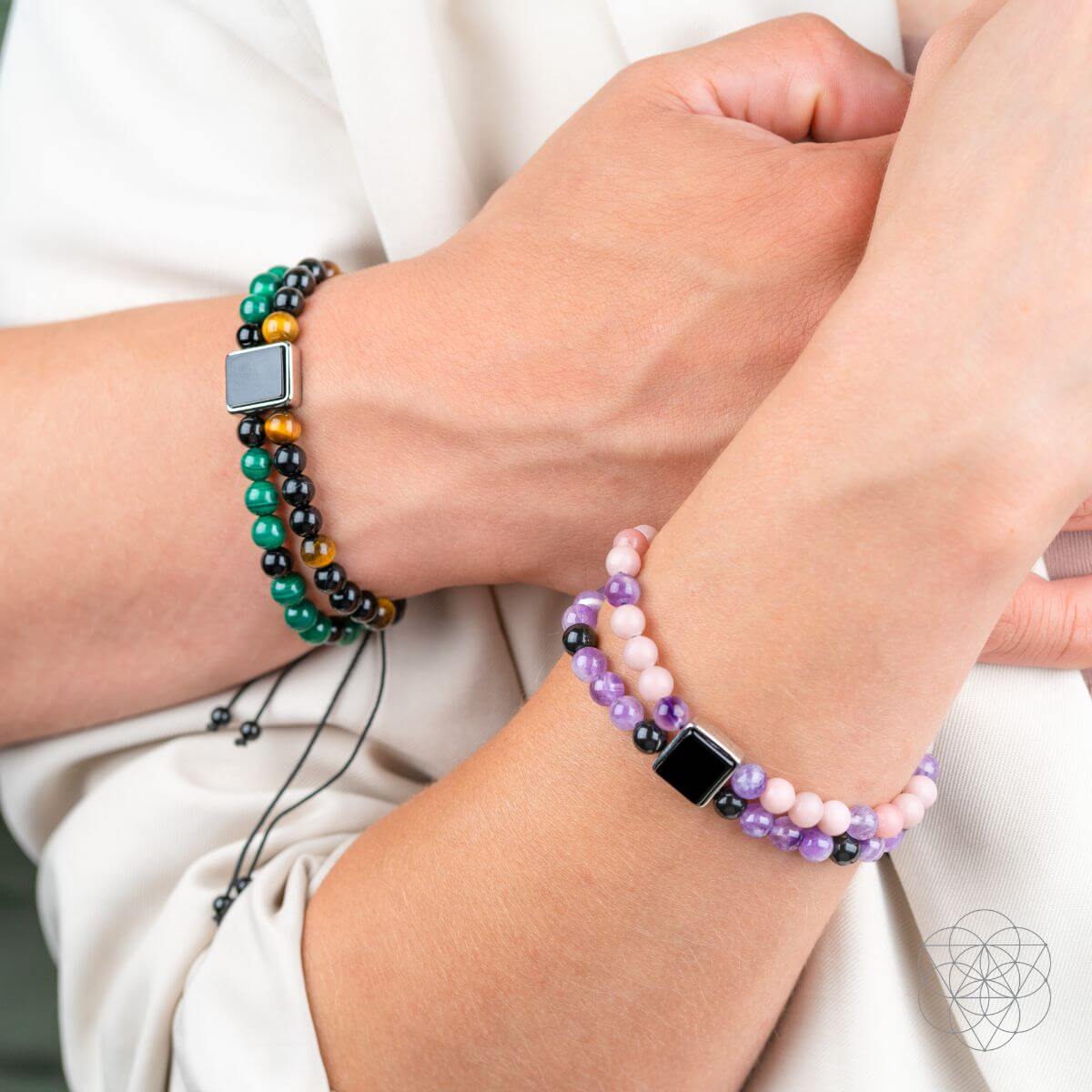 Two hands wearing beaded bracelets on a plain background