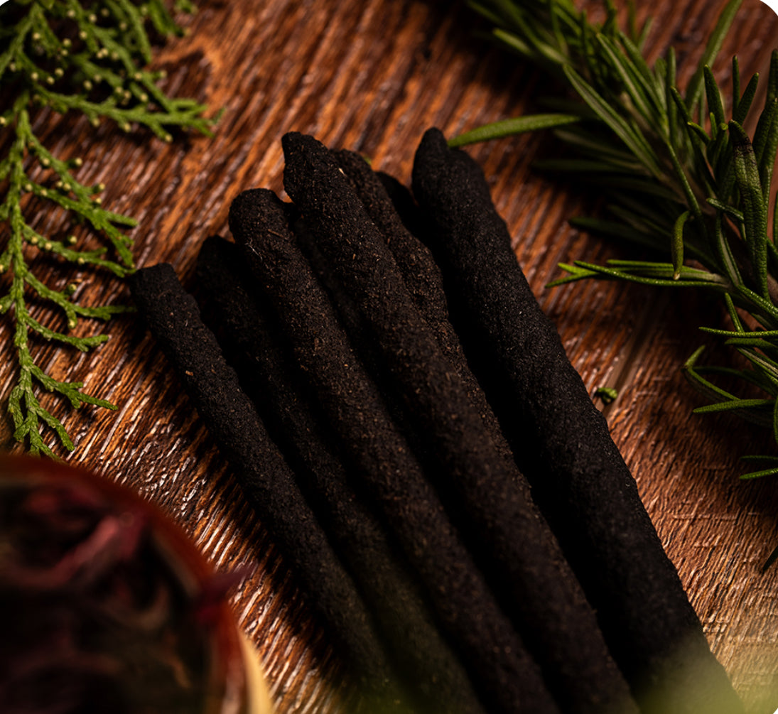 Dark incense sticks on a wooden surface with green leaves