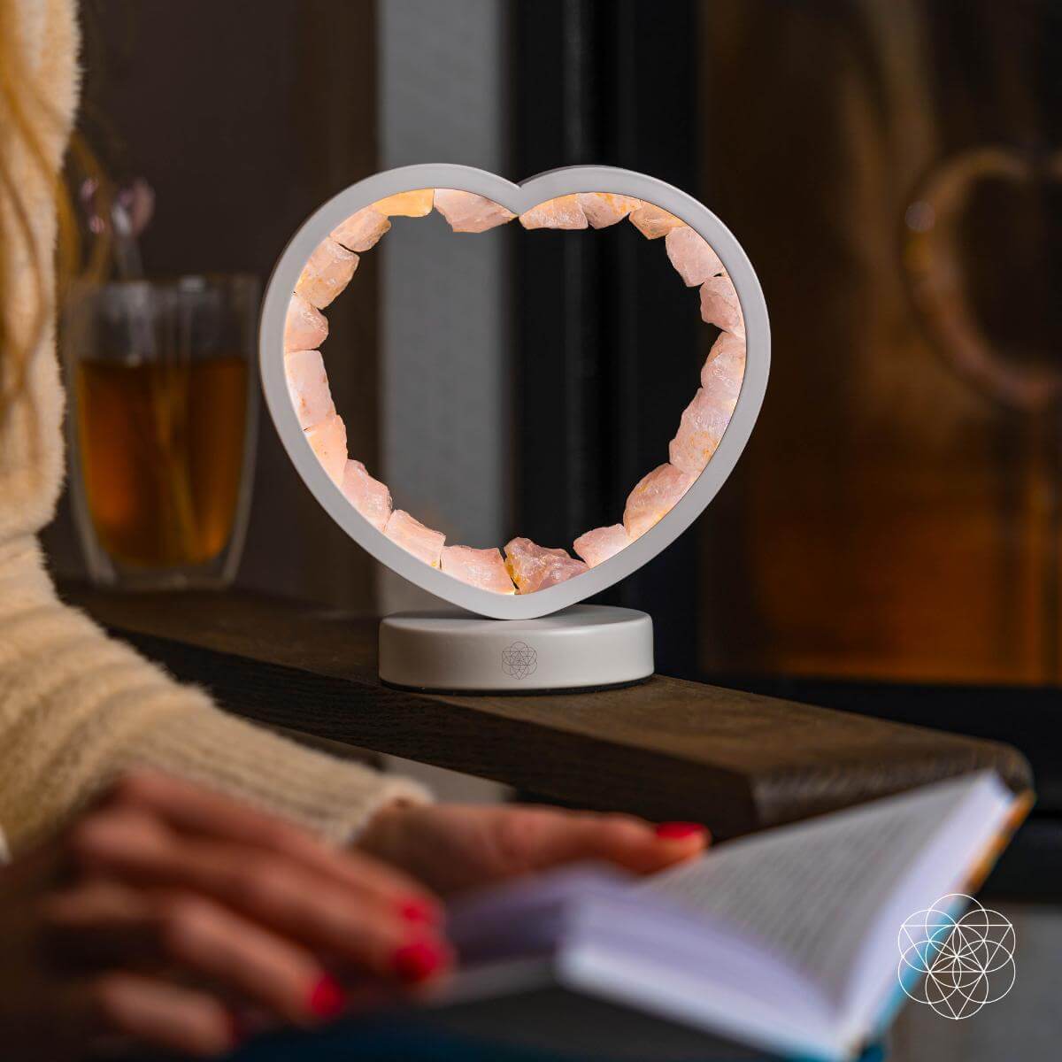 Heart-shaped lamp on a table with a person reading a book in a cozy setting.