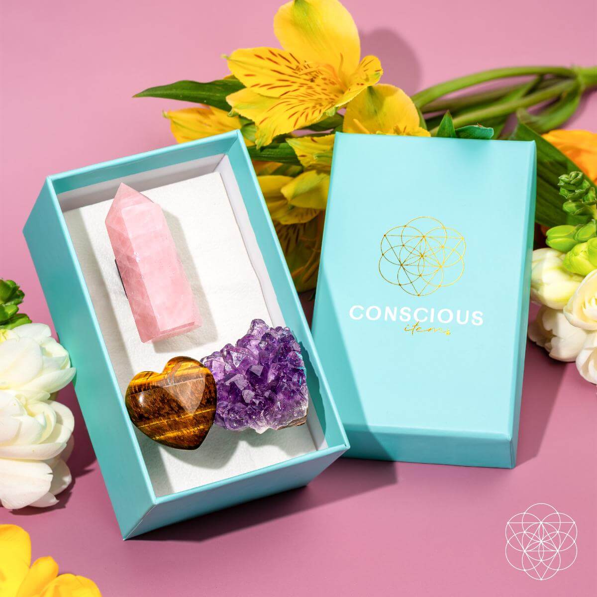Turquoise box with pink and brown crystal-like objects and amethyst, against a pink background with flowers.