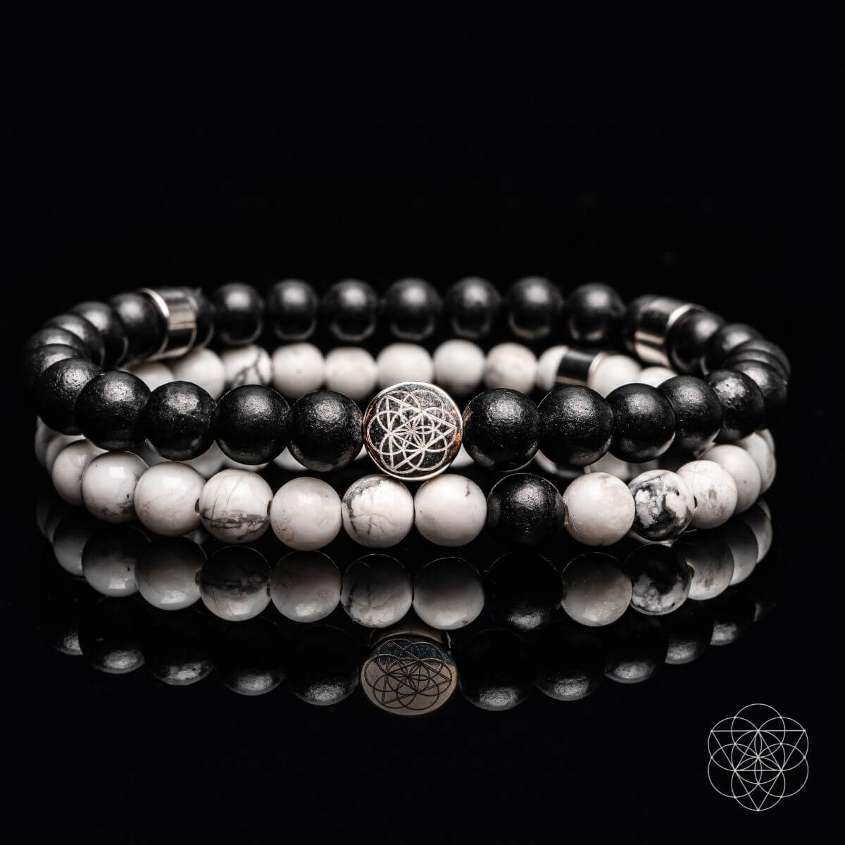 Stack of black and white beaded bracelets with a silver charm on a reflective surface.