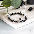 Stack of black and white beaded bracelets on a marble surface with green leaves and stones.