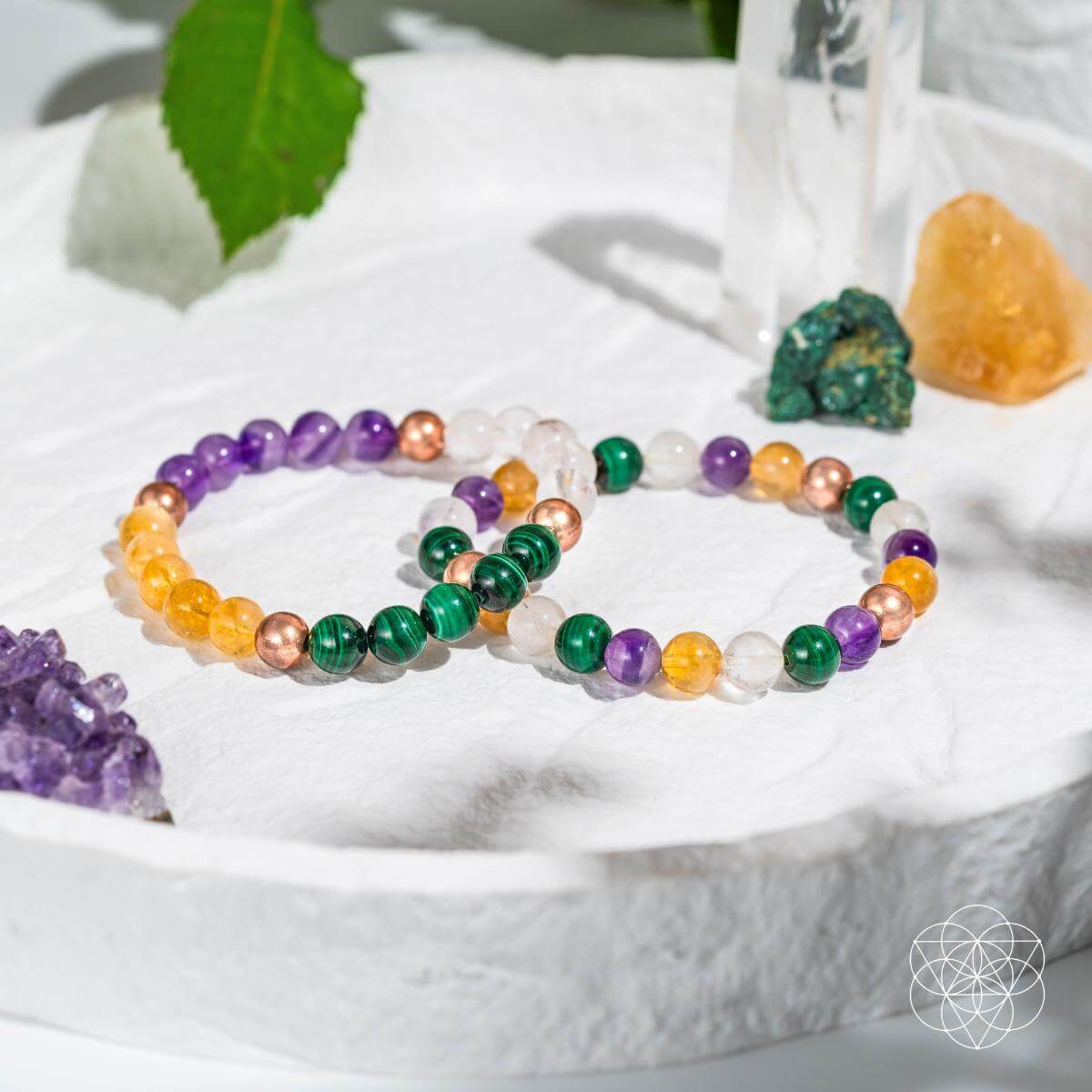 Colorful beaded bracelets on a white surface with crystals and leaves.
