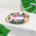 Colorful beaded bracelets on a white surface with green leaves in the background