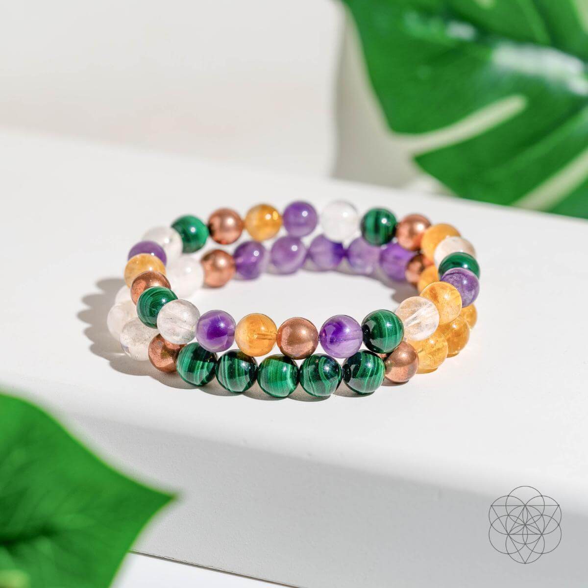 Colorful beaded bracelets on a white surface with green leaves in the background