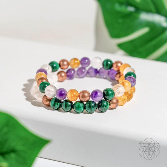 Colorful beaded bracelets on a white surface with green leaves in the background