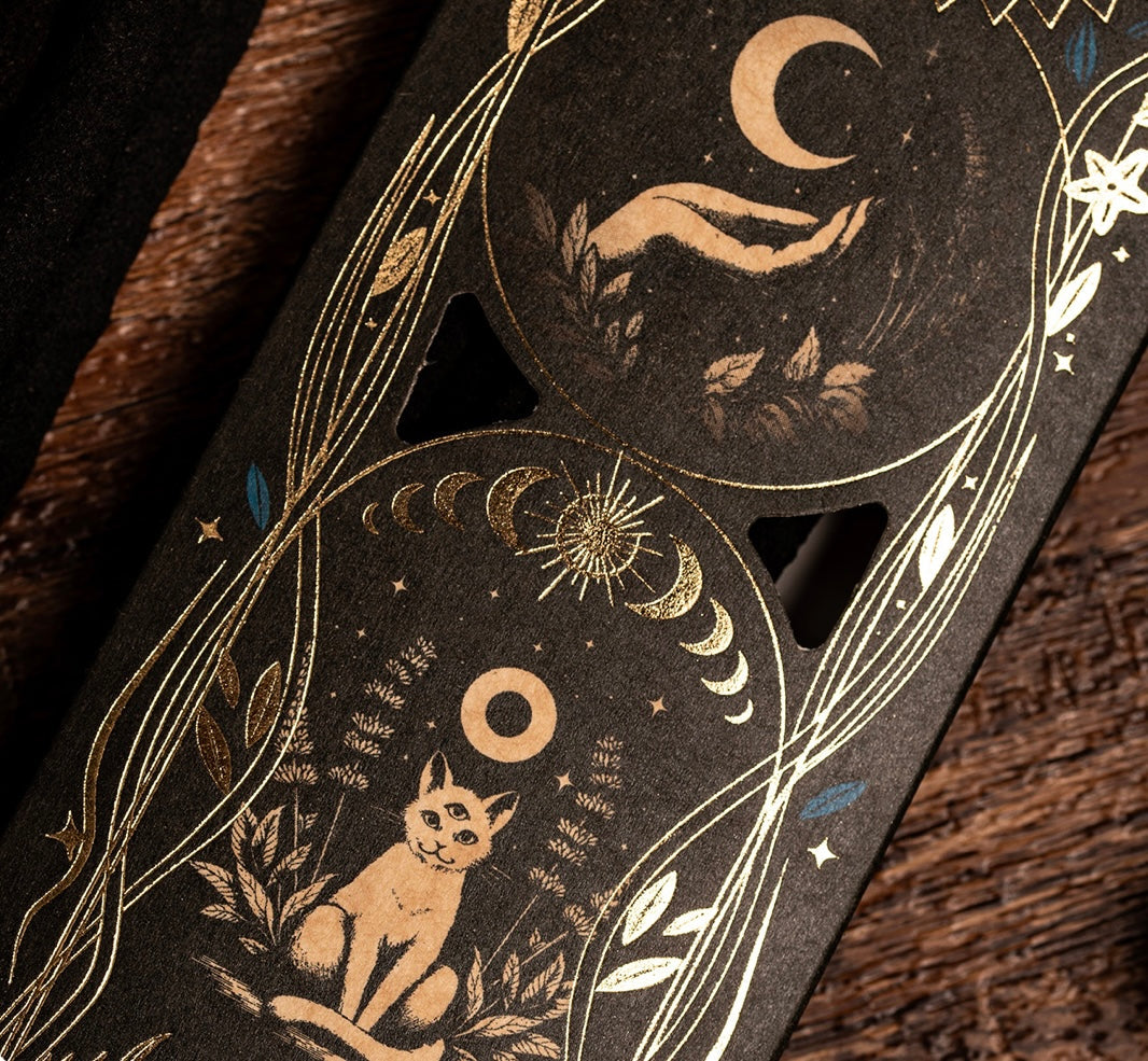 Decorative object with celestial designs, including cats, moon, and stars, on a dark background.