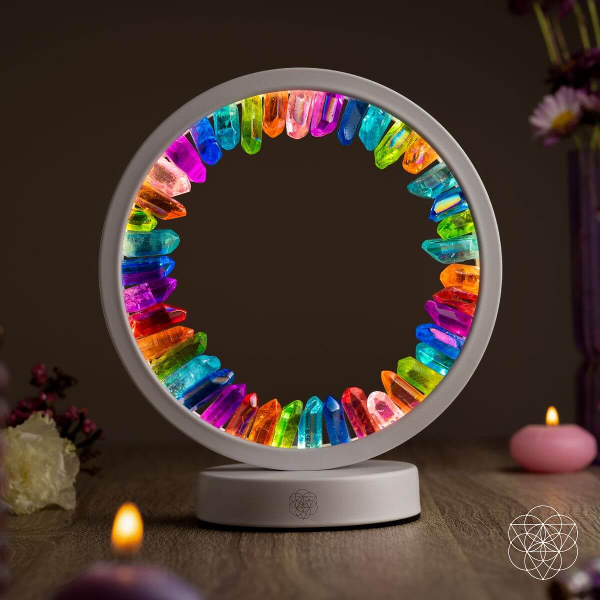 Circular light fixture with colorful crystals on a wooden surface with candles and flowers.