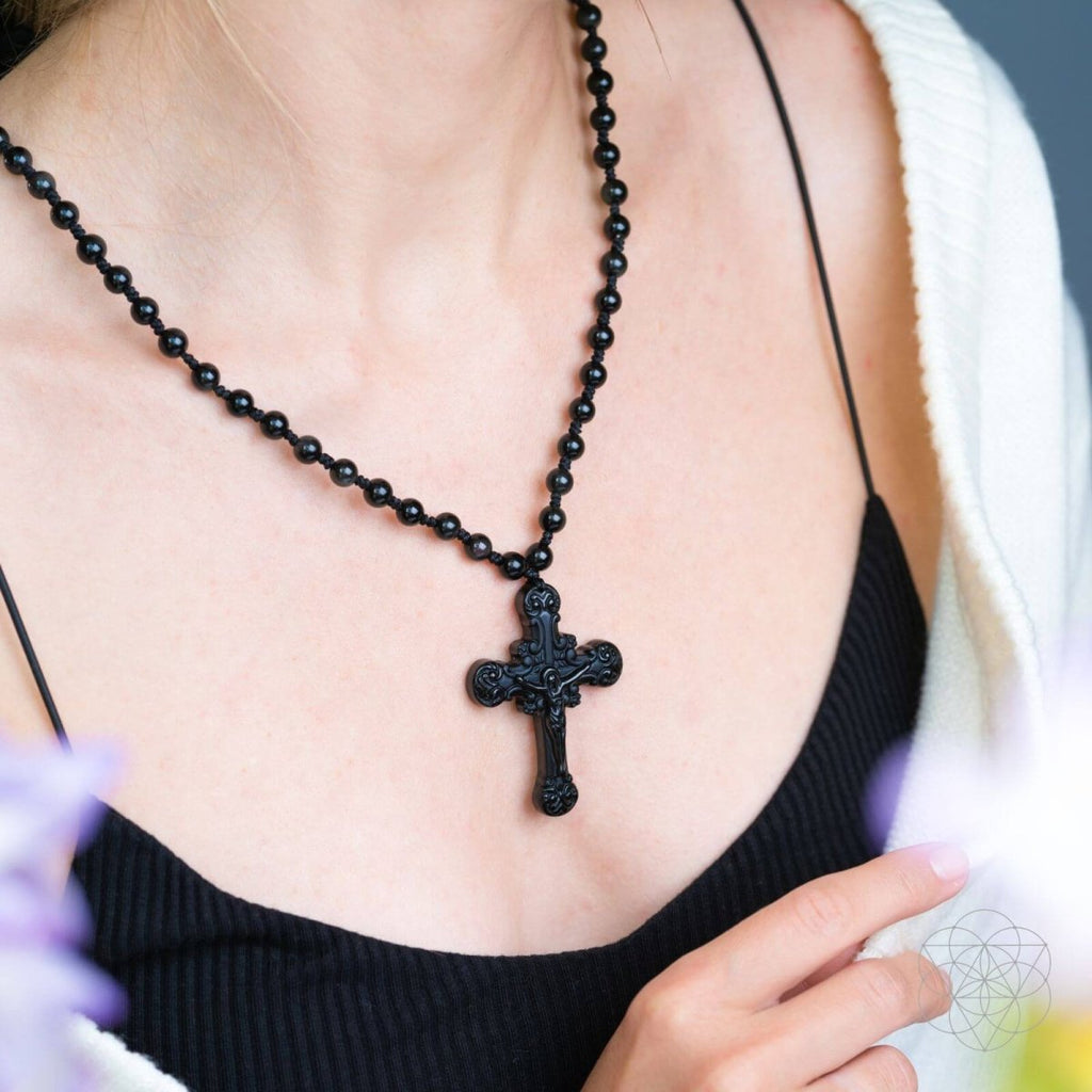 Black beaded necklace with a cross pendant worn by a person