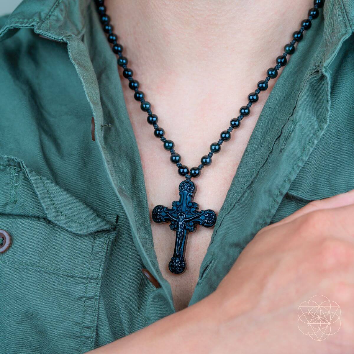 Person wearing a green shirt with a black beaded necklace and cross pendant.