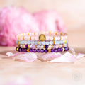 Stack of beaded bracelets with a central emblem on a soft pink background
