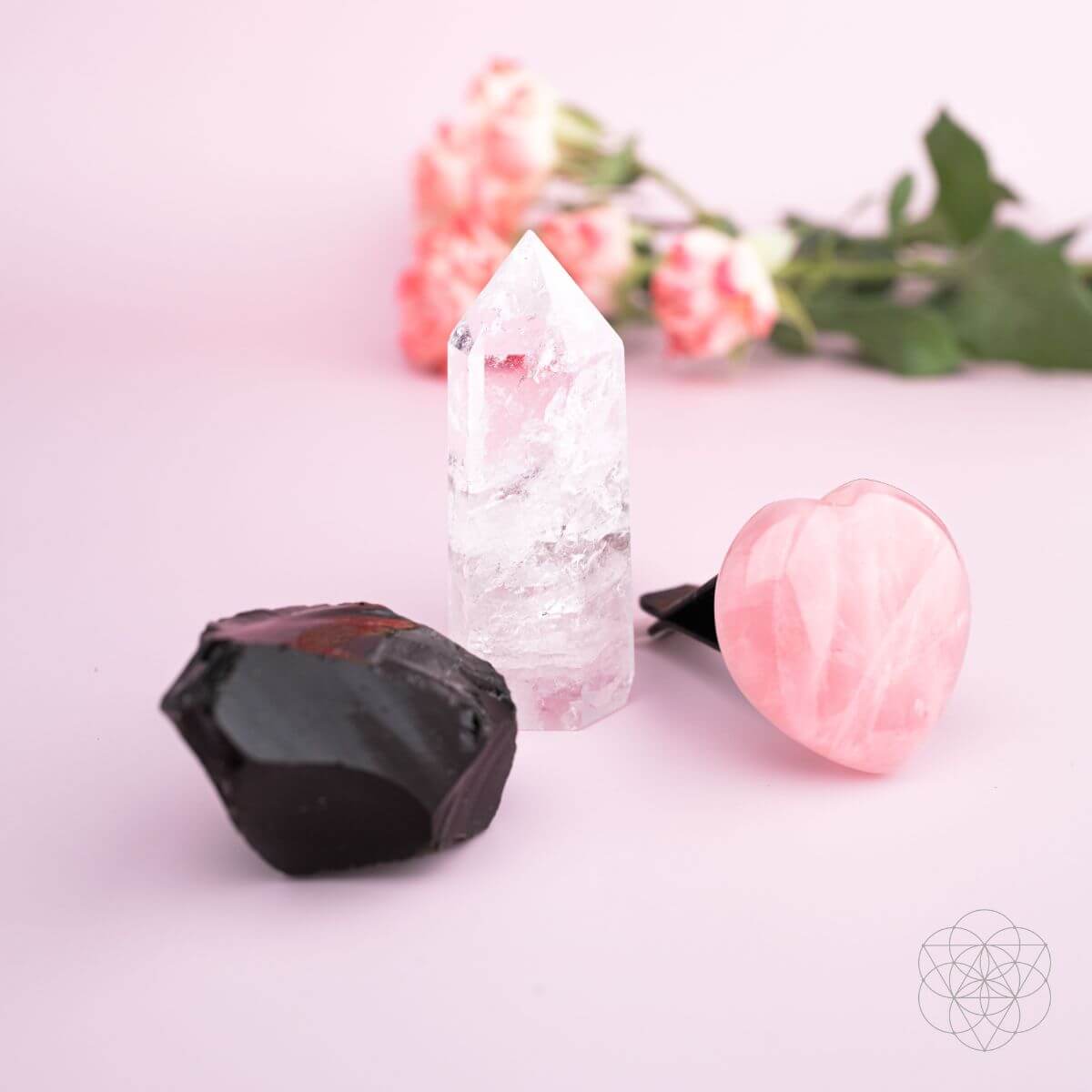 Three crystals on a light pink surface with blurred flowers in the background