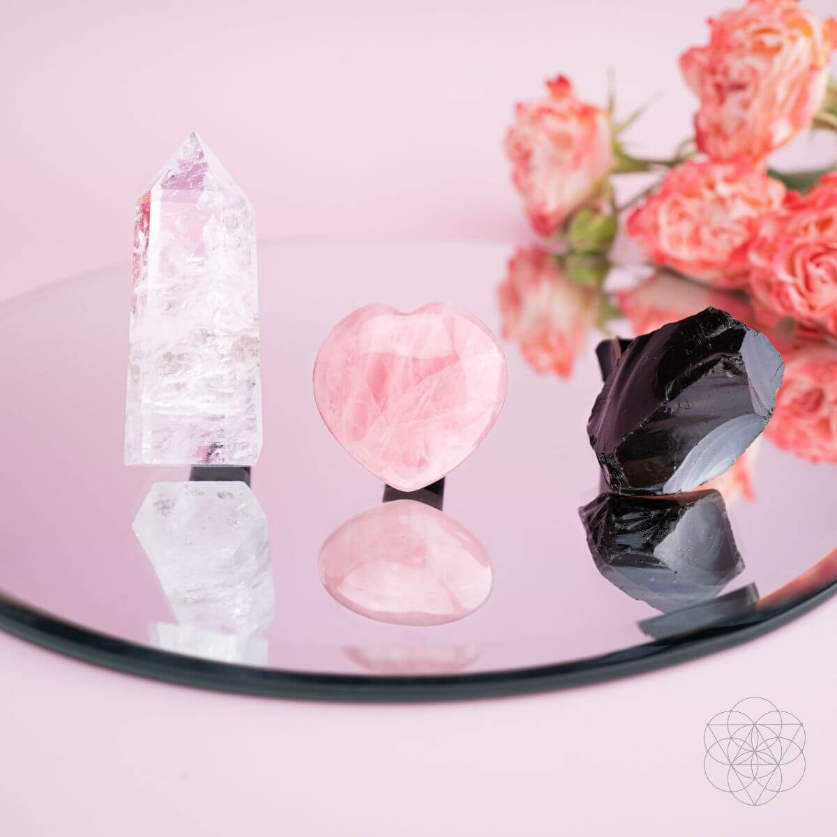 Crystal objects on a reflective surface with pink flowers in the background