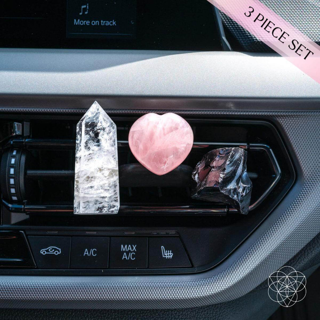 Three crystal objects on a car's air vent with a pink ribbon and text overlay.
