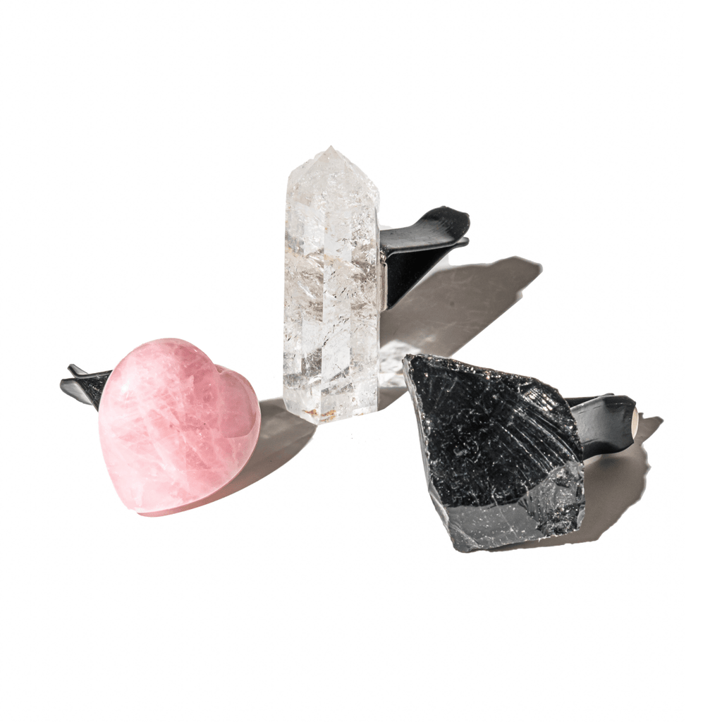 Three crystals on a white background: a pink crystal, a clear crystal, and a black crystal.