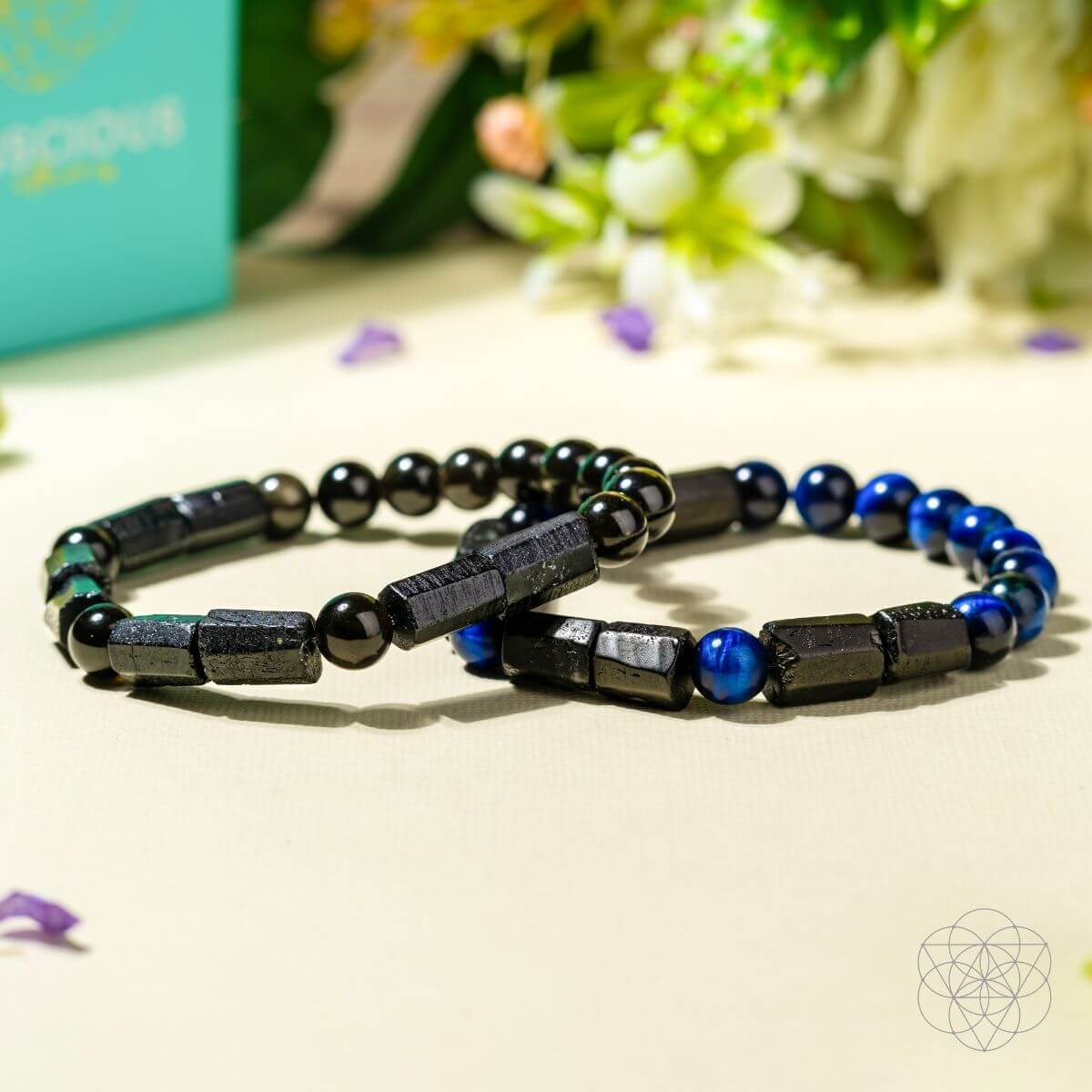Two beaded bracelets with black and blue beads on a light surface with a blurred natural background.