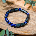 Bracelet with blue and black beads on a wooden surface with greenery