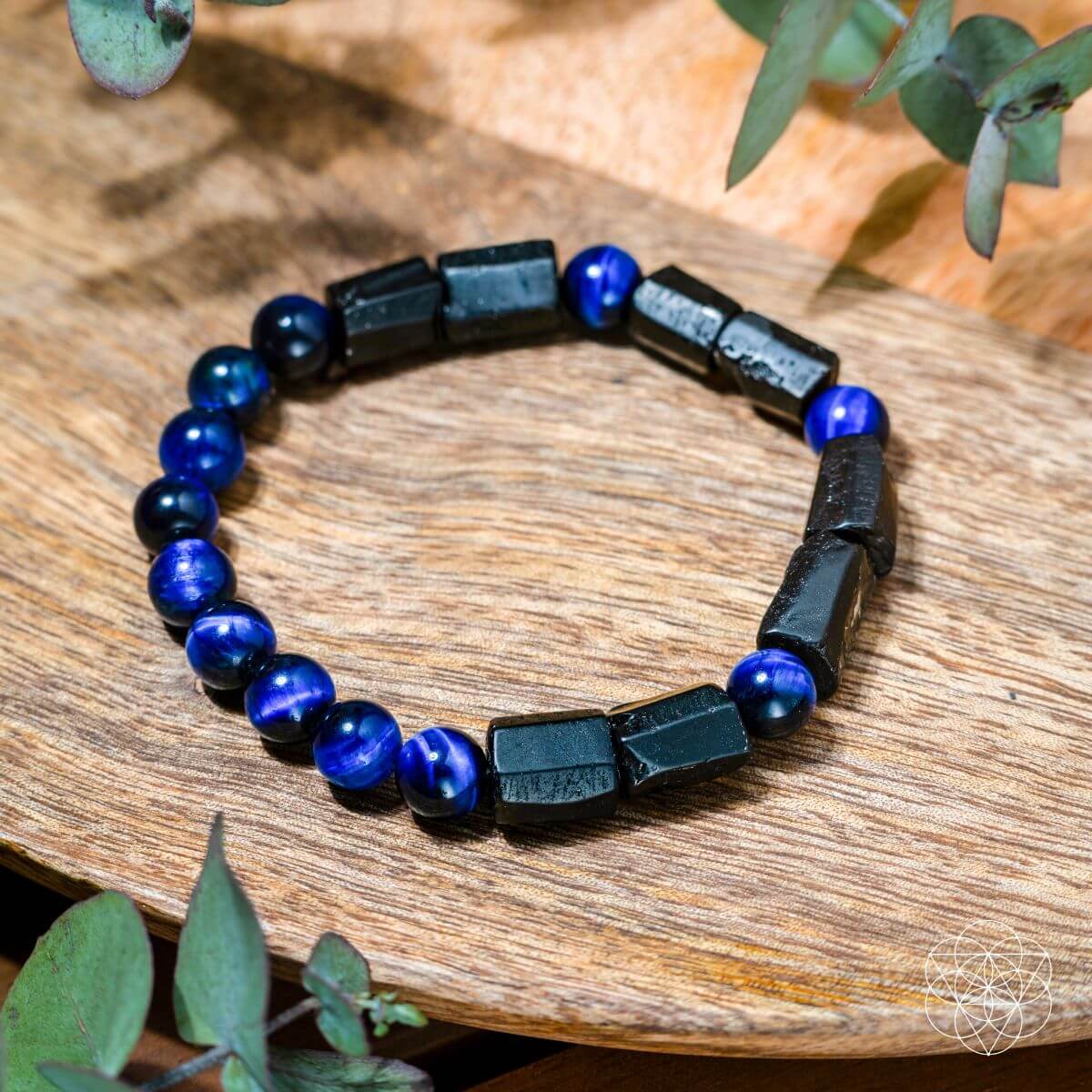 Bracelet with blue and black beads on a wooden surface with greenery