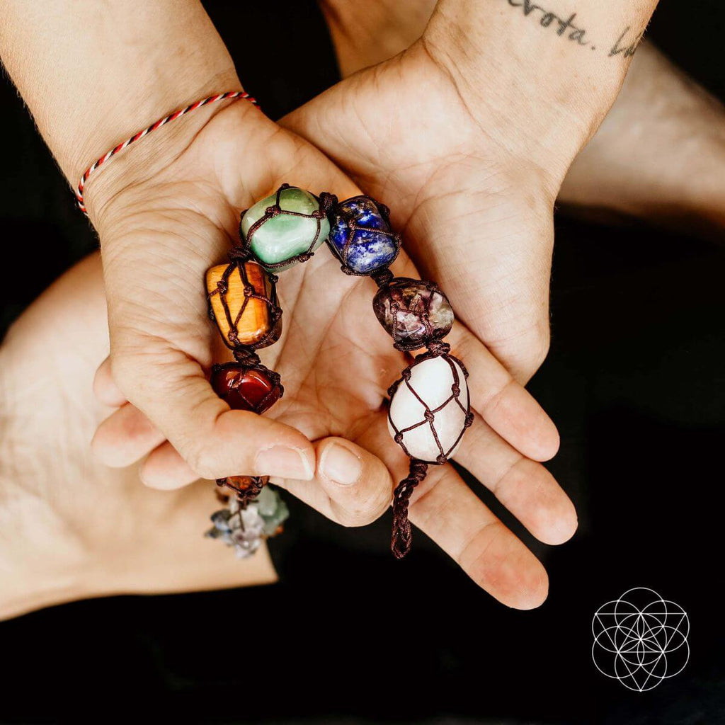 Hands holding a colorful crystal bracelet against a dark background