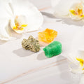 Three colorful crystals on a light wooden surface with white flowers in the background.