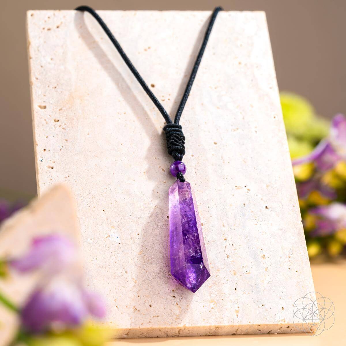 Amethyst pendant necklace on a white stand with blurred flowers in the background