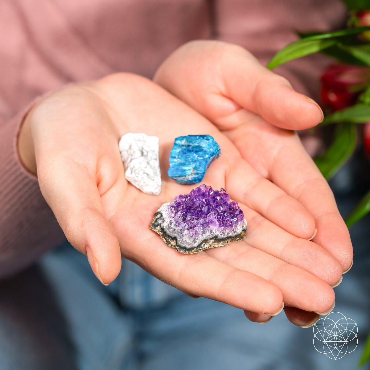 Hands holding three colorful crystals: white, blue, and purple.