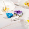 Three colorful crystals on a light surface with flowers in the background