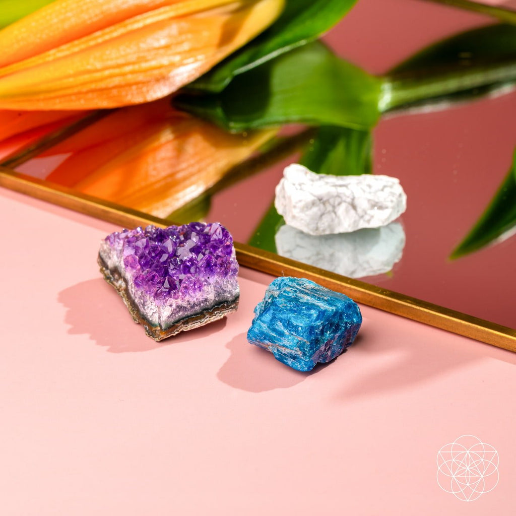 Three colorful crystals on a reflective surface with a floral background