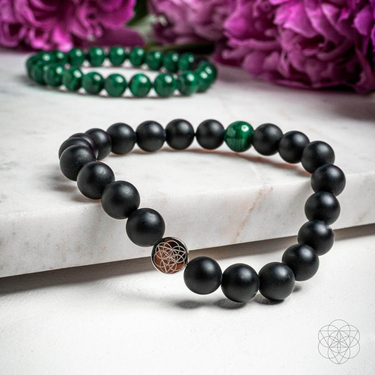 Black beaded bracelet with a rose gold charm on a marble surface with purple flowers in the background