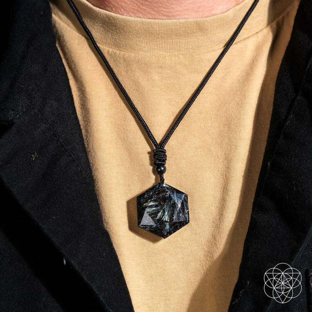 Black pendant necklace on a person wearing a beige shirt and black jacket.
