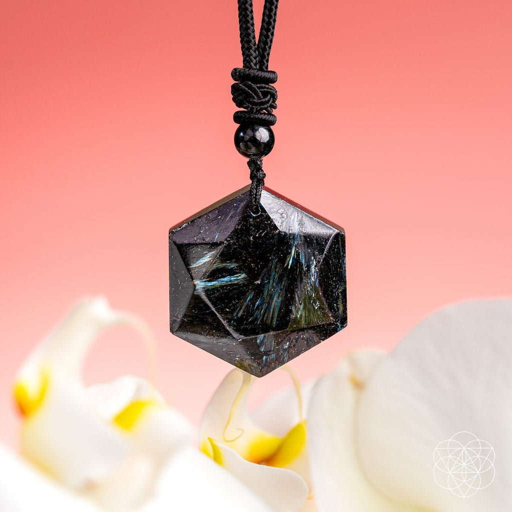 Hexagonal crystal pendant on a cord with a pink background and flowers in the foreground