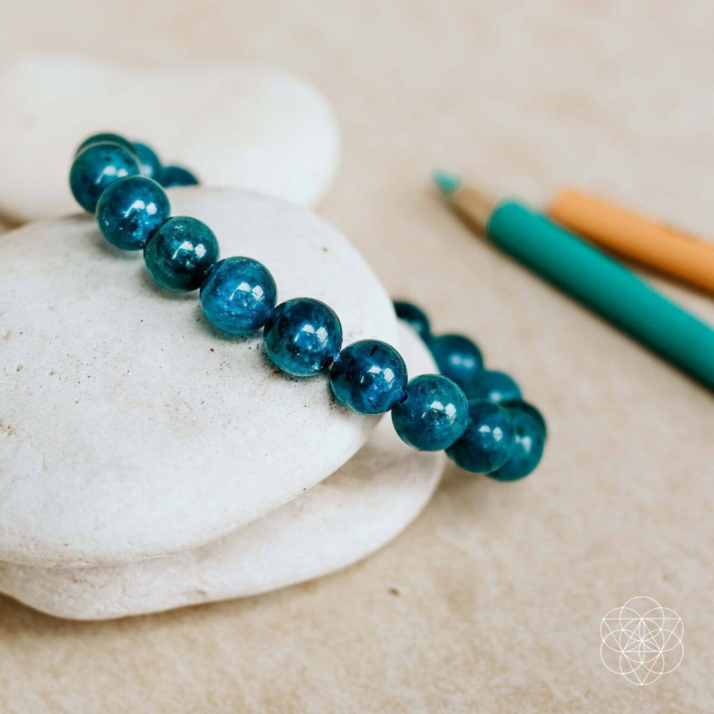 Blue beaded bracelet on a white stone with a pencil and pen in the background