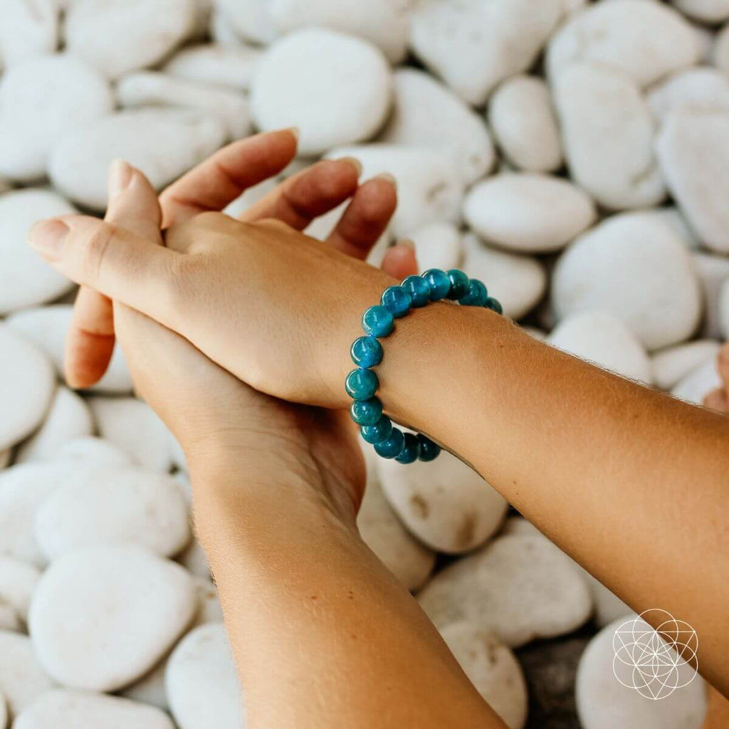 Person wearing a blue beaded bracelet with pebbles in the background