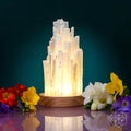 Crystal lamp with a wooden base on a reflective surface with flowers around it.