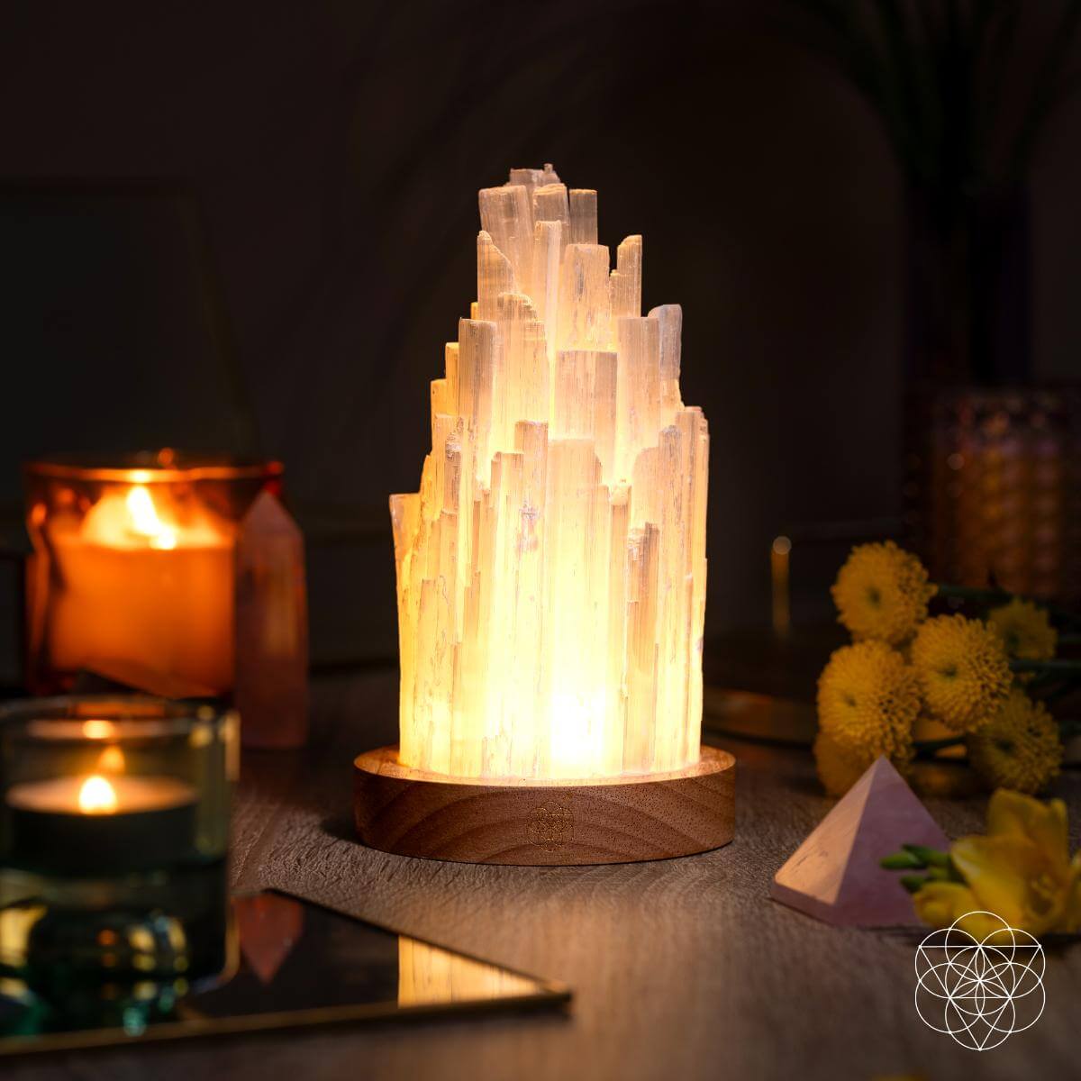 Selenite crystal tower lamp on a wooden base with candles and flowers in the background.
