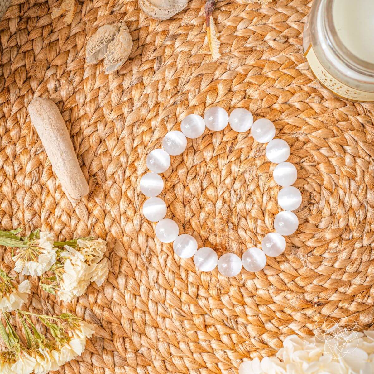 Pearl bracelet on a woven surface with flowers and a candle
