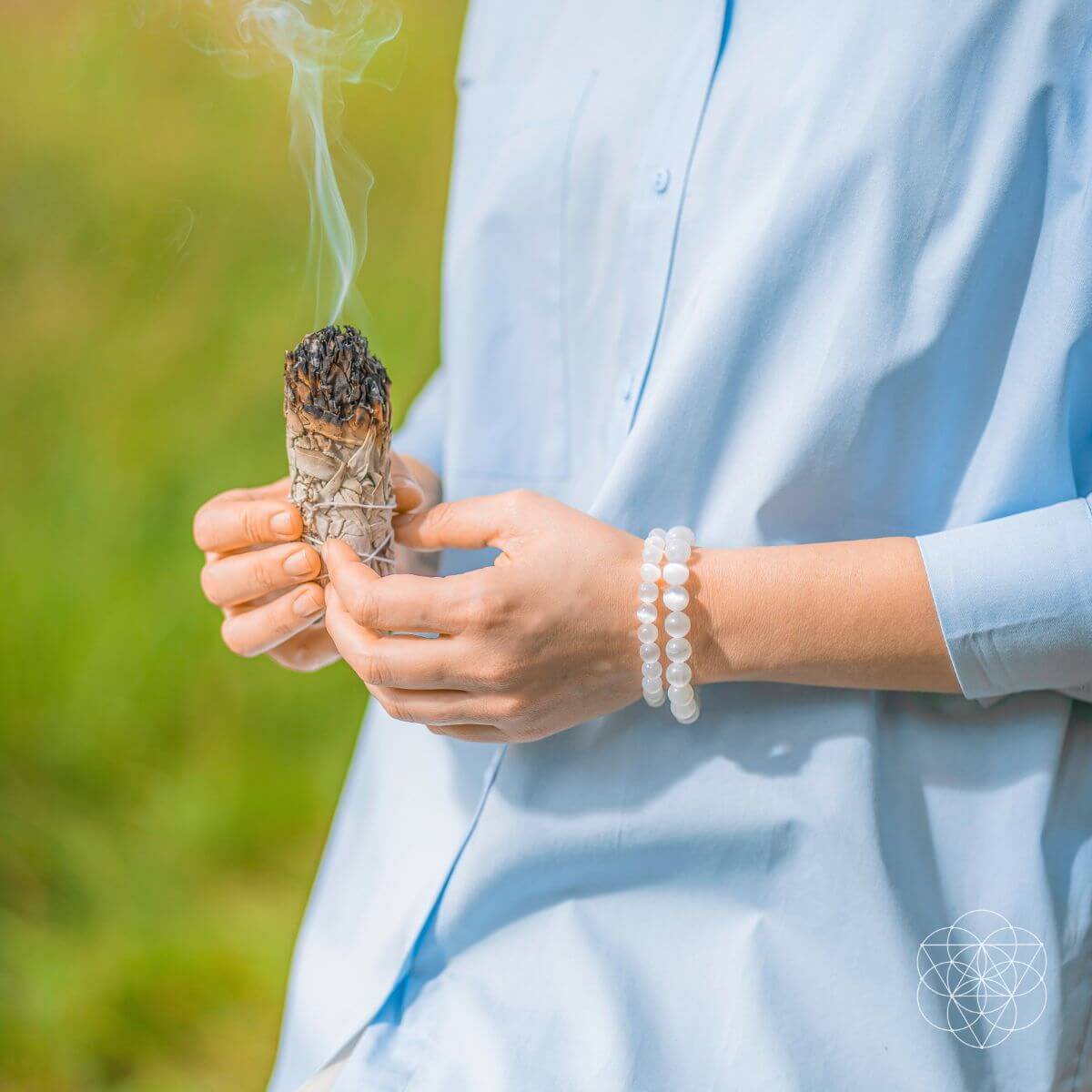 Person holding a smoldering sage stick outdoors with a blurred natural background