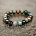 A beaded stretch bracelet made of polished multicolored gemstone-like round beads, arranged in a circle on a textured gray surface.