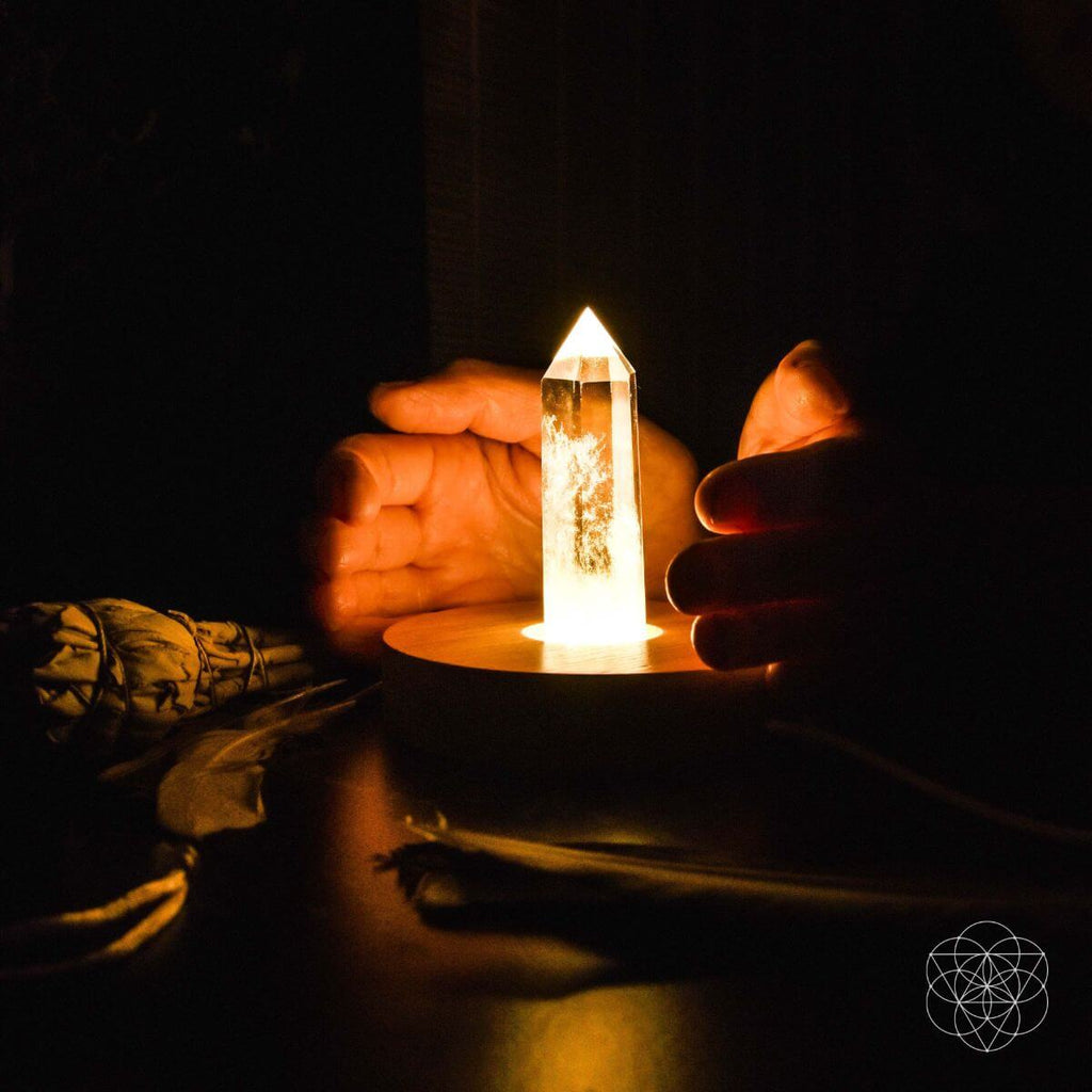Crystal tower held by hands in a dark setting with a smoldering sage bundle.