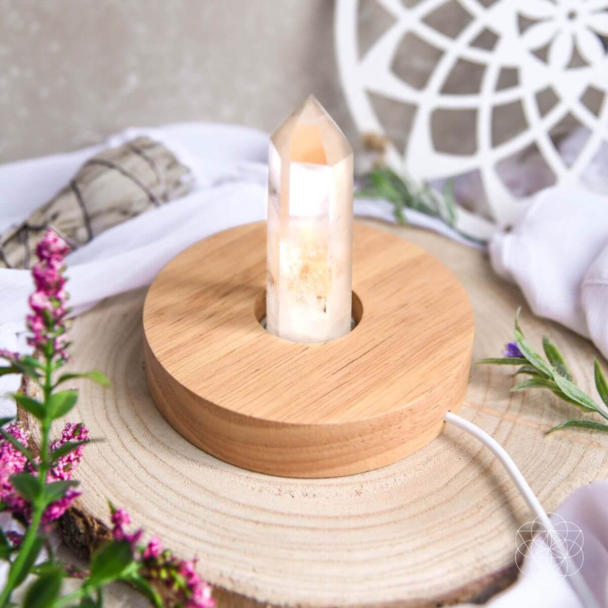 Wooden lamp with a candle-like light source on a wooden base, surrounded by flowers and fabric.