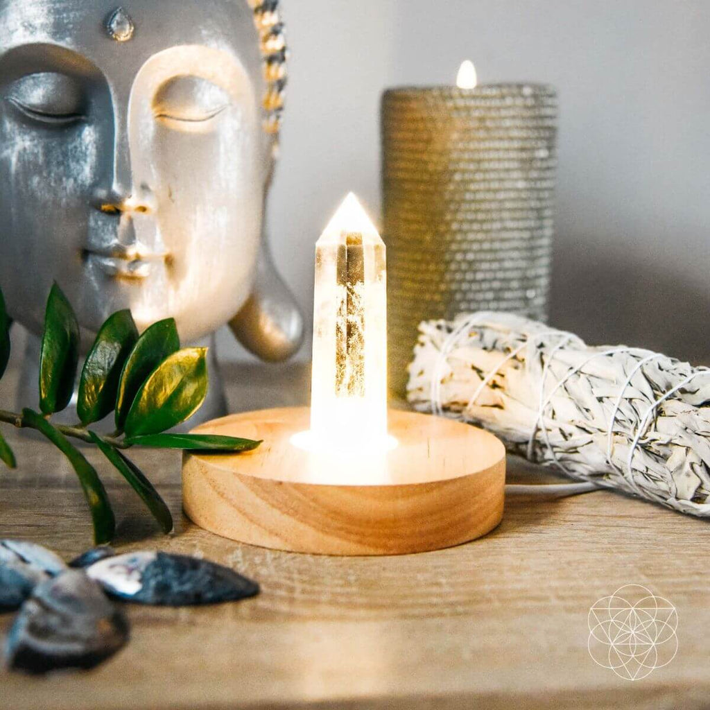 Crystal lamp on a wooden surface with a Buddha statue, candle, and sage in the background.